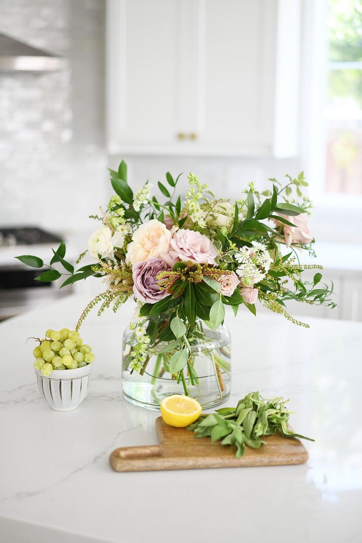 a vase filled with flowers sitting on top of a counter next to a cutting board