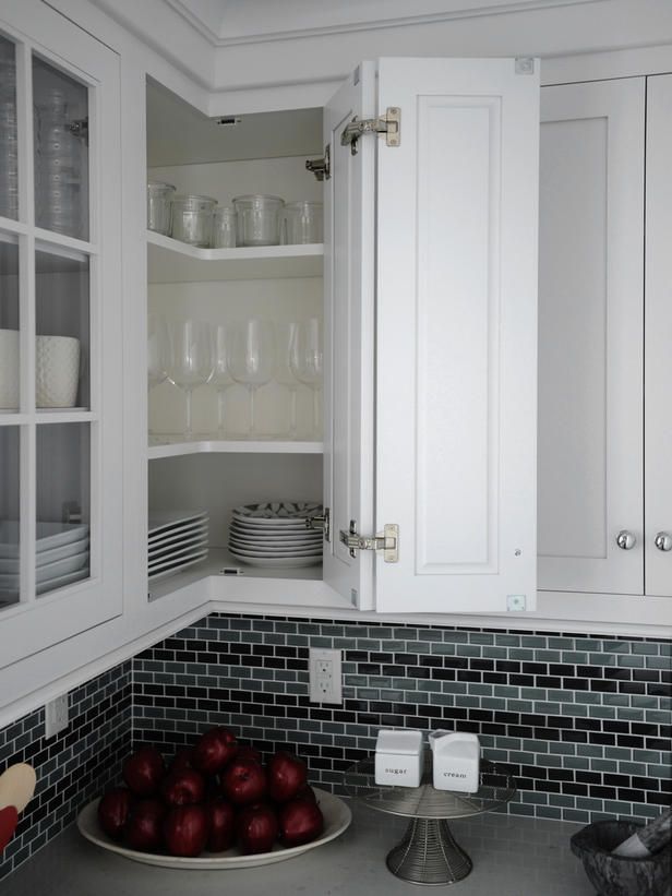 a bowl of apples is on the counter in this white kitchen with black tile and glass cabinets