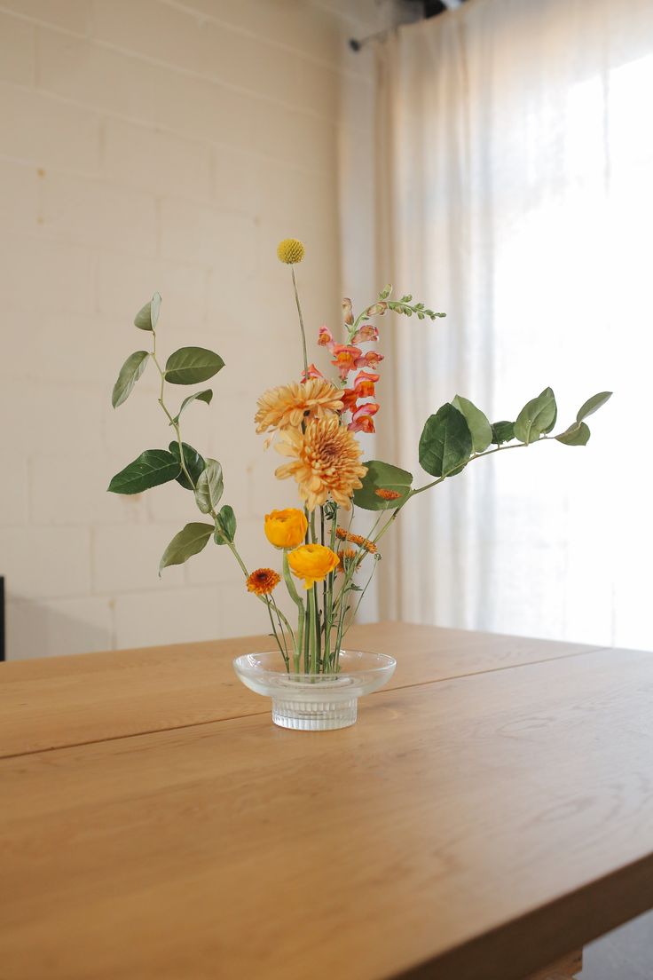 a glass vase filled with yellow flowers on top of a wooden table next to a window