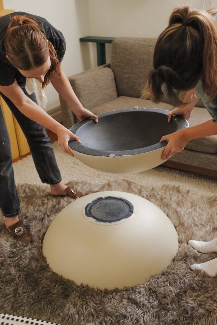 two women are bending over to put something in a pan on top of the floor