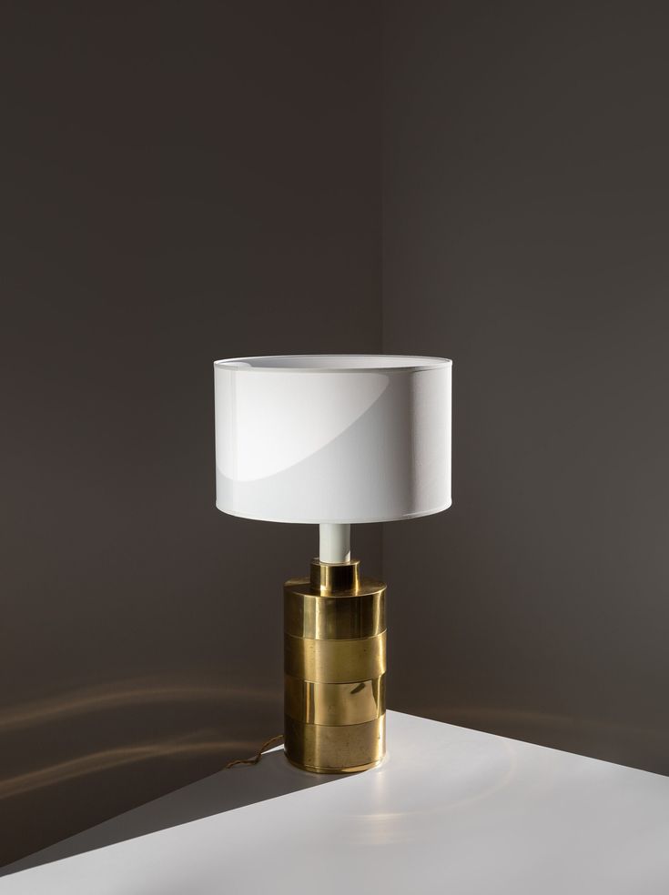 a table lamp with a white shade on it's base and a gold plated metal body