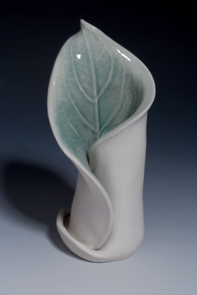 a white vase with a green leaf in the center and an upside down design on it