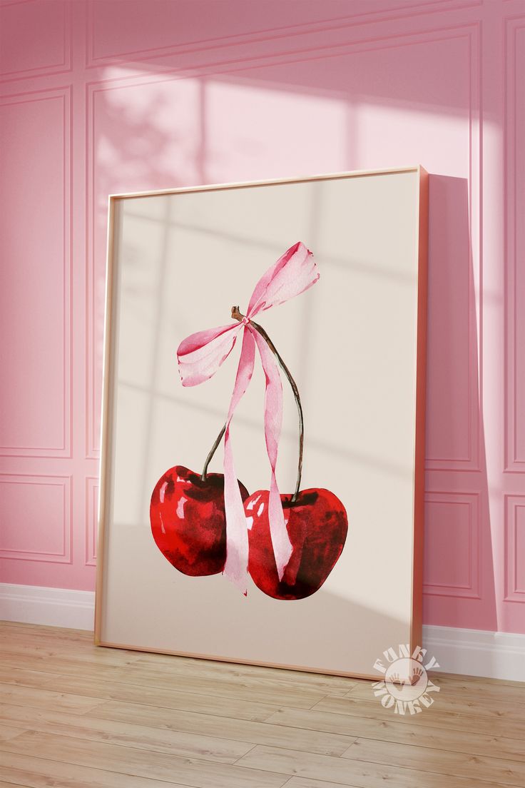 two cherries hanging on a pink wall in front of a white frame with ribbon