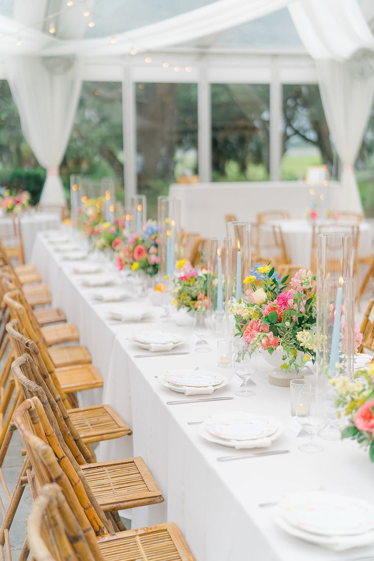 a long table is set up with white linens and floral centerpieces for an outdoor wedding reception