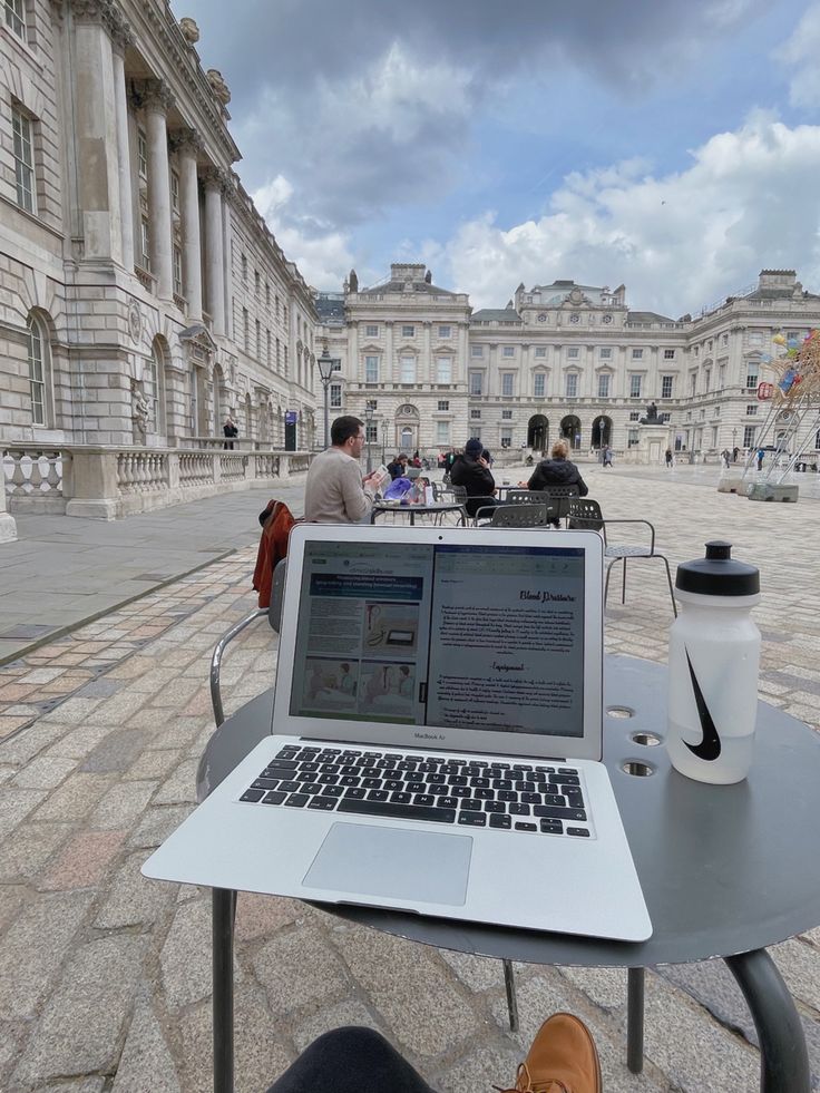 an open laptop computer sitting on top of a table in front of a large building