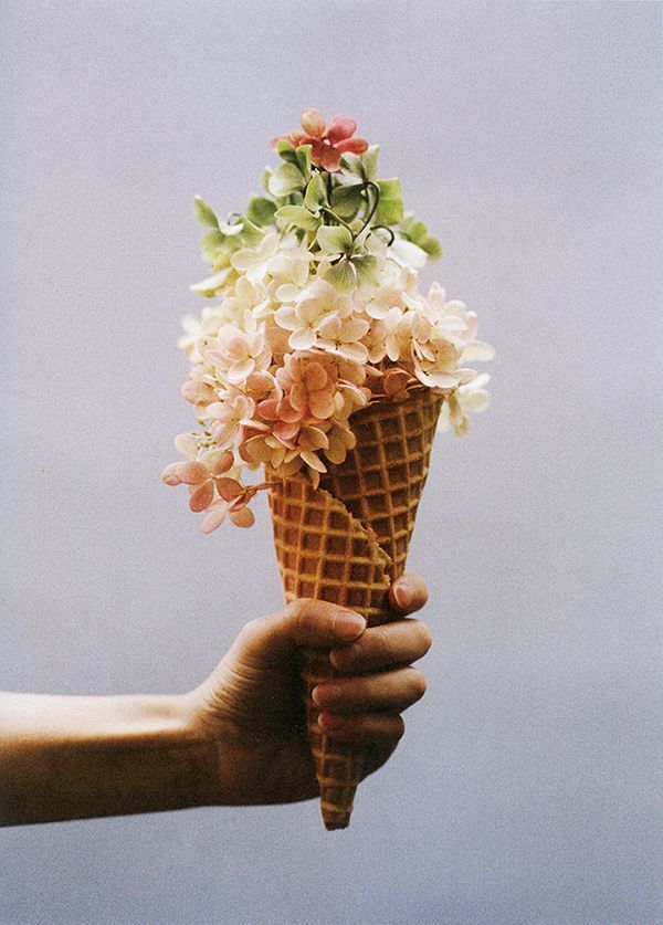 a person holding an ice cream cone with flowers in it