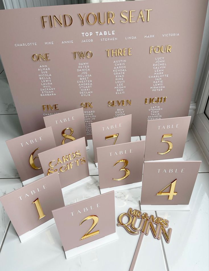 table numbers and place cards are displayed on a white tablecloth with gold foil lettering