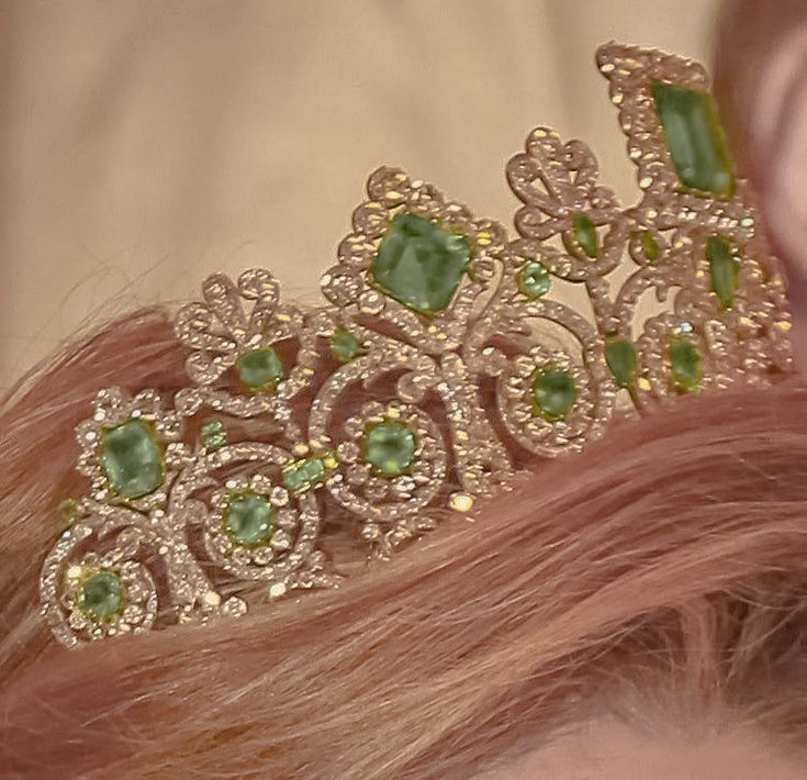 a close up of a woman wearing a tiara with green stones on it's head