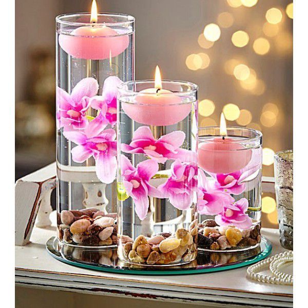 three glass vases filled with pink flowers and rocks on a tray next to candles