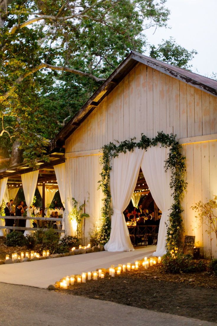 an outdoor wedding venue with candles lit up in front of the entrance to the barn