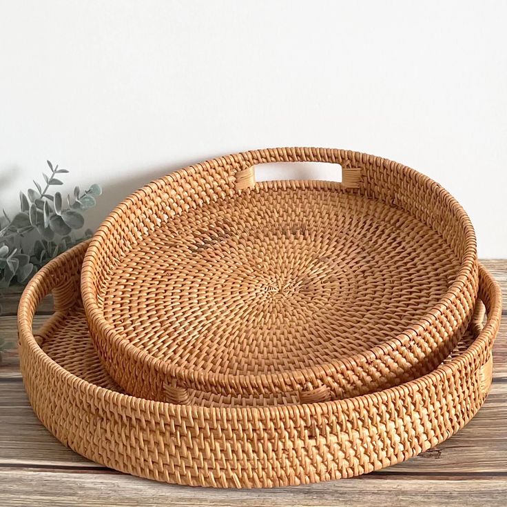 two round woven baskets sitting on top of a wooden table next to a potted plant
