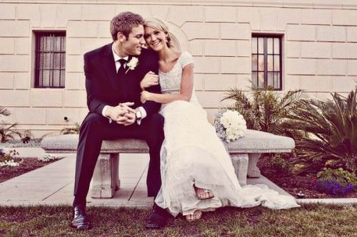 a bride and groom sitting on a bench in front of a building