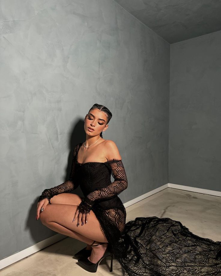 a woman sitting on the floor in a room with grey walls and black lace dress