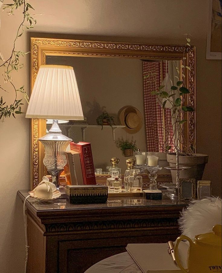 a mirror sitting on top of a dresser next to a lamp and table with books