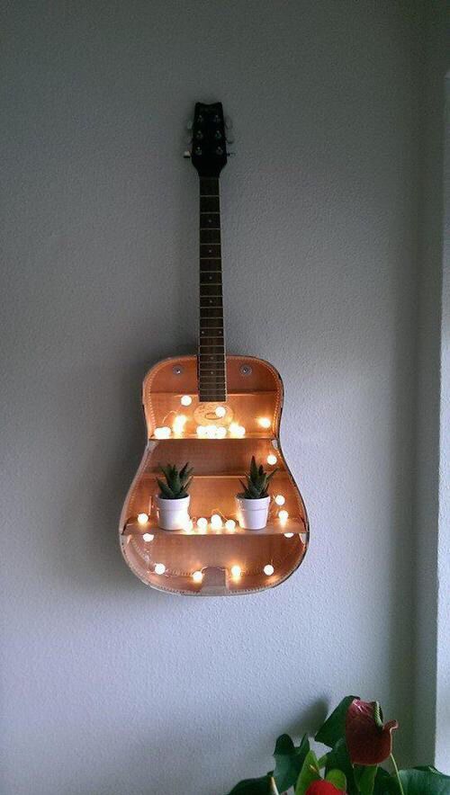 a guitar shaped planter hanging from the side of a wall with lights on it