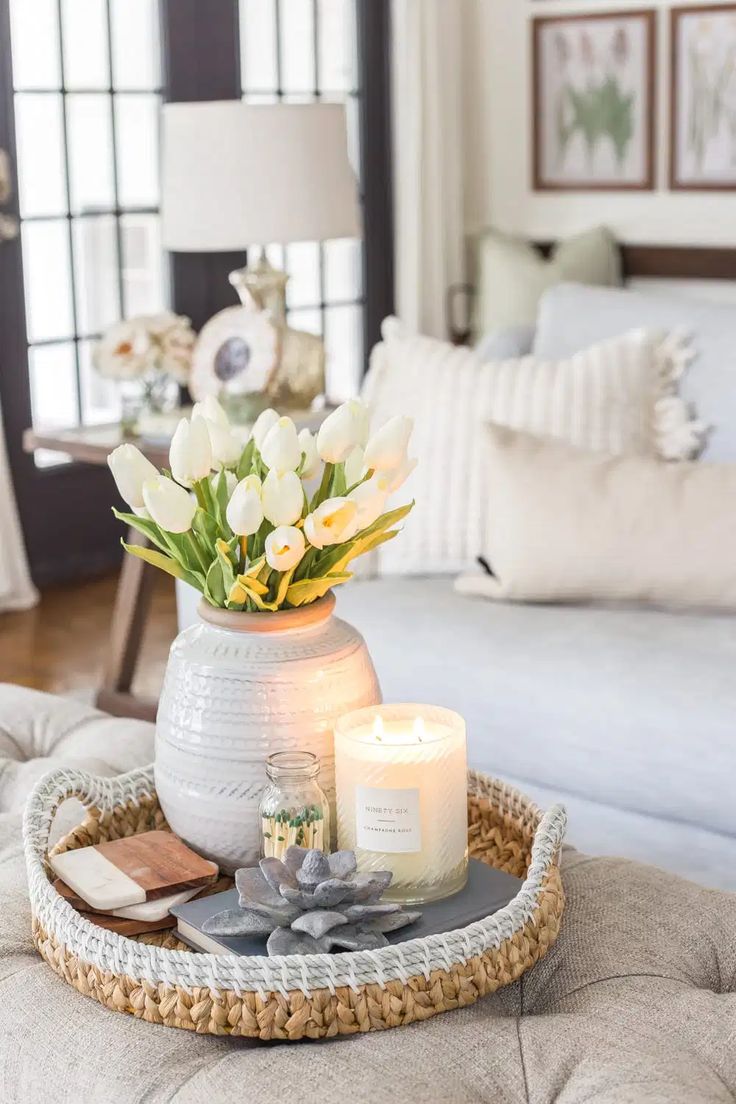 a tray with flowers and candles on top of a couch in a living room next to a window
