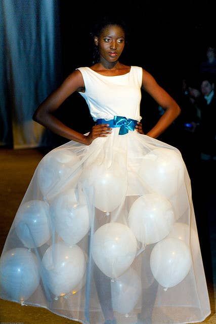 a woman in a white dress with balloons on the runway at a fashion week event