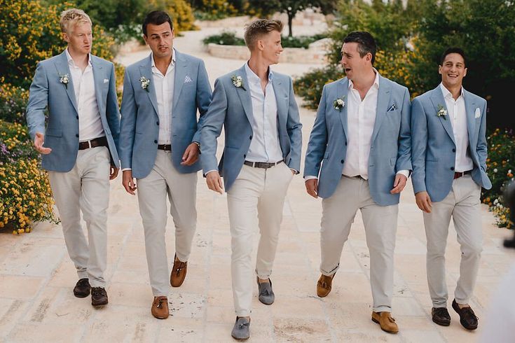 a group of men in suits walking down a sidewalk together with one man wearing a white shirt and tan pants