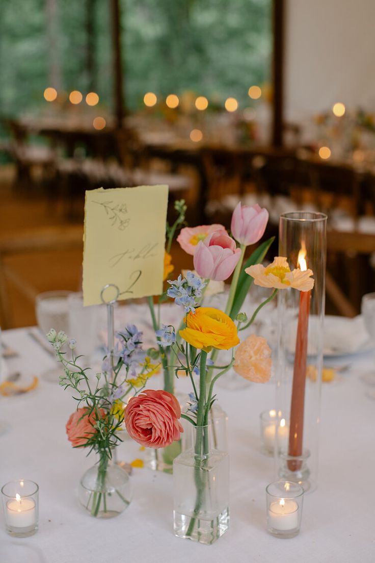 flowers in vases on a table with candles and note pinned to the wall behind them