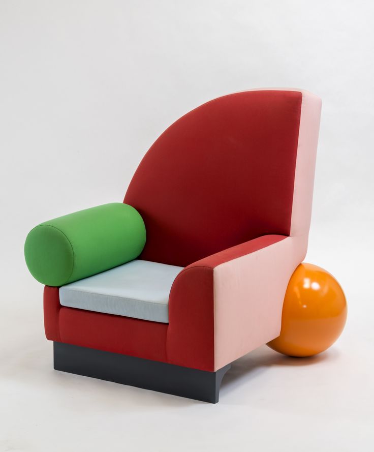 an orange ball sitting next to a red and green chair on a white surface with the seat up