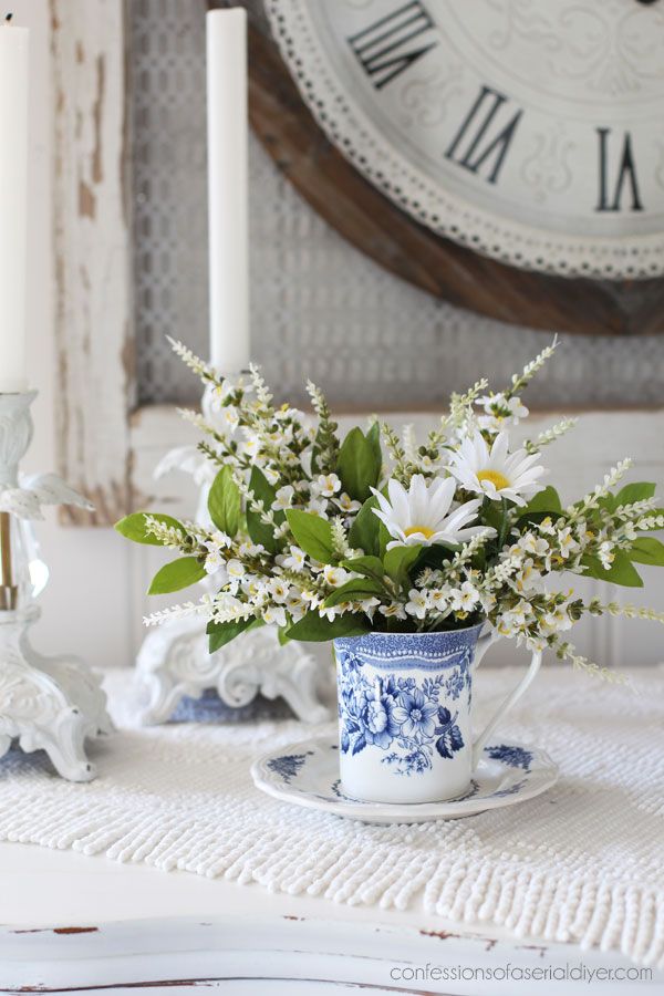 a blue and white vase filled with flowers sitting on top of a table next to a clock