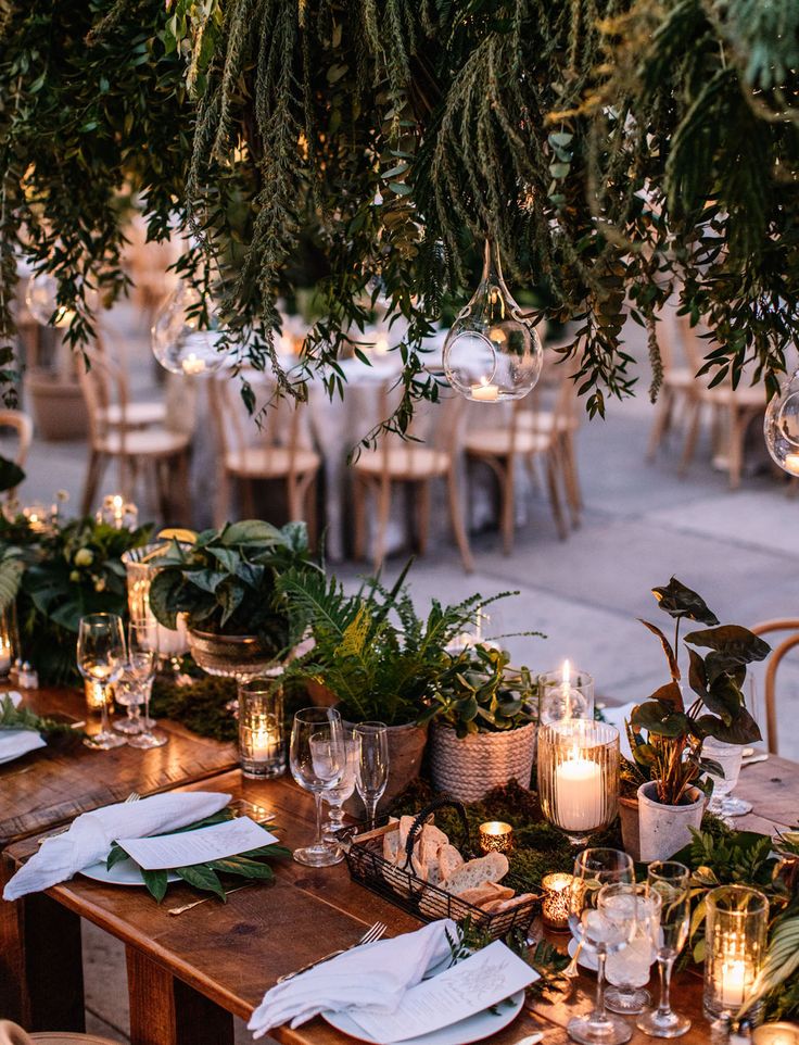 an outdoor table set with candles and greenery