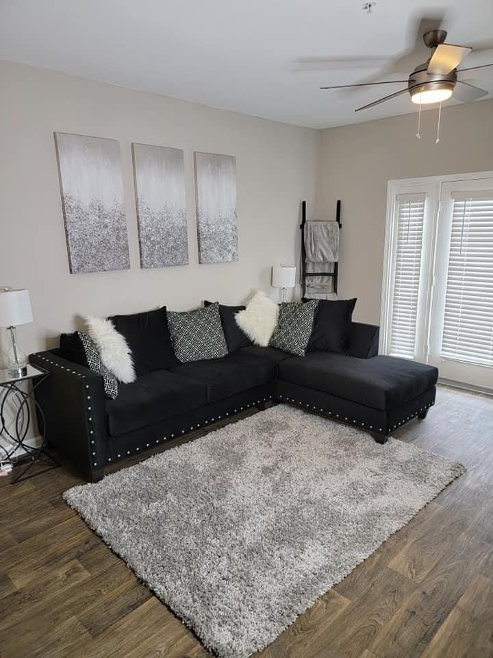 a living room with black couches and white rugs on the hardwood flooring