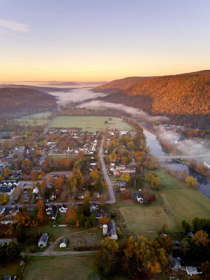 an aerial view of a small town surrounded by mountains and trees in the fall season