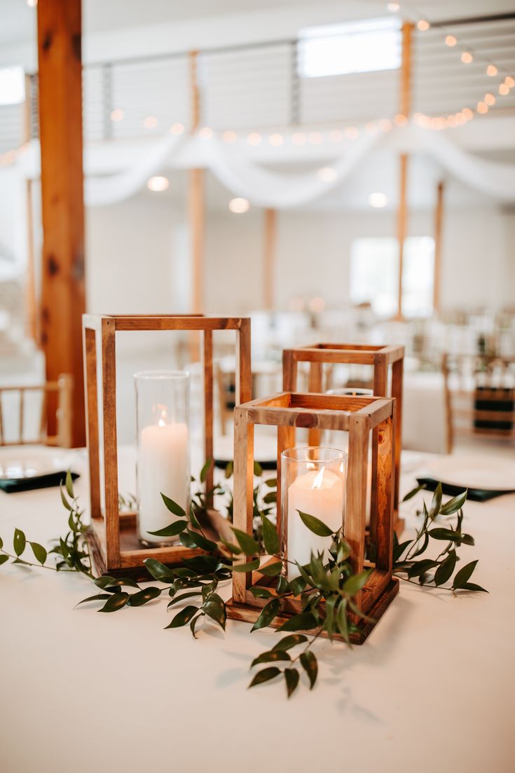 two lanterns with greenery and candles on top of the table at a wedding reception