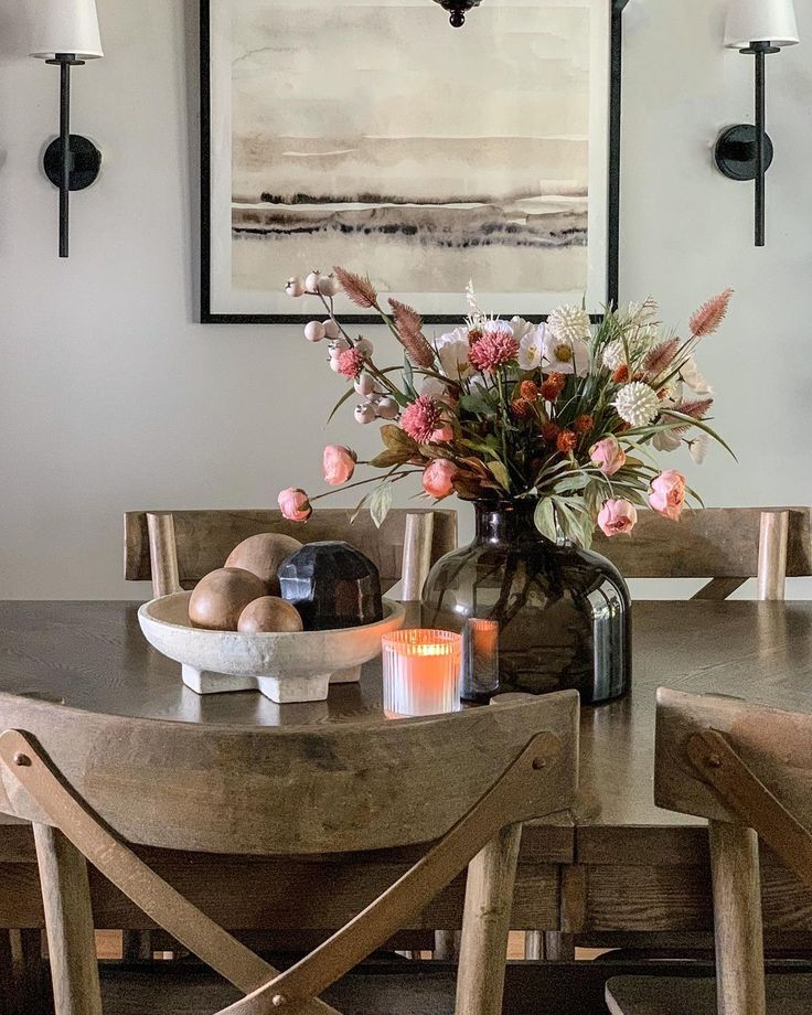 a dining room table with flowers in a vase and candles on the table next to it