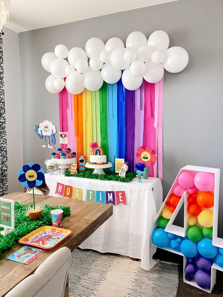 a birthday party with balloons, streamers and rainbow decorations on the table in front of it