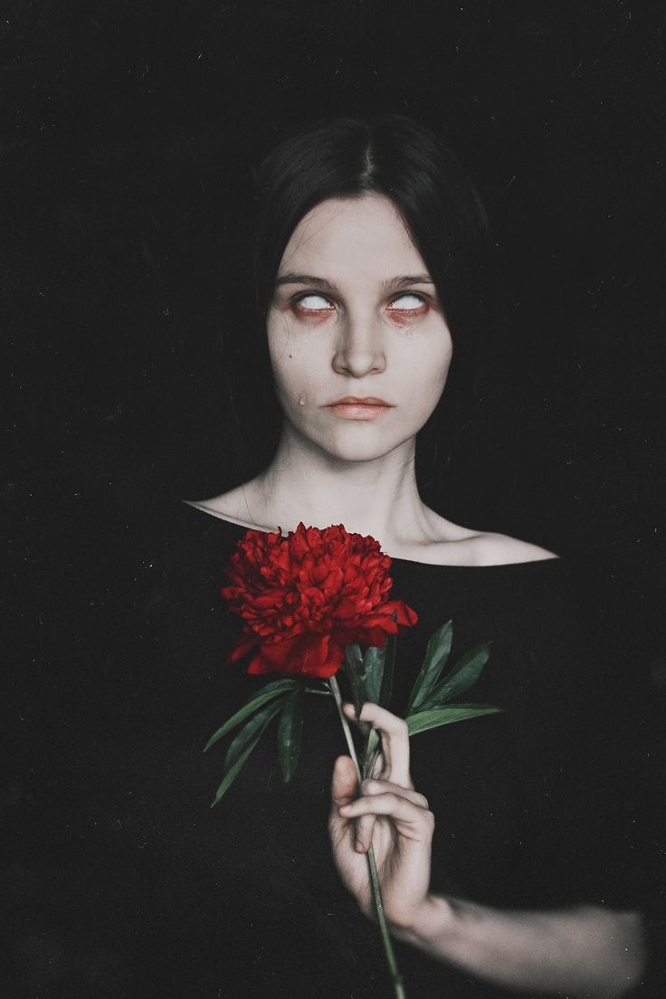 a woman holding a red flower in her right hand and looking at the camera with an evil look on her face
