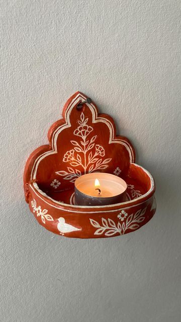 a candle is lit in an orange and white bowl hanging from the wall with a flower design on it