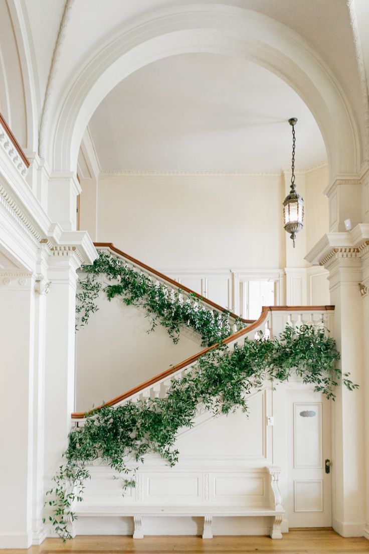 the stairs are covered with green plants and hanging from the railings in an elegant room