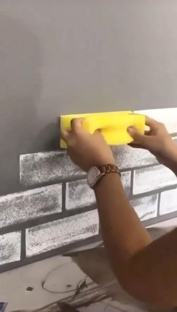 a person using a sponge to paint a brick wall with gray and white tiles on it