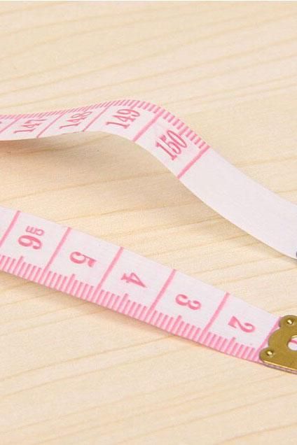 a pink and white measuring tape with a teddy bear on it's end next to a ruler