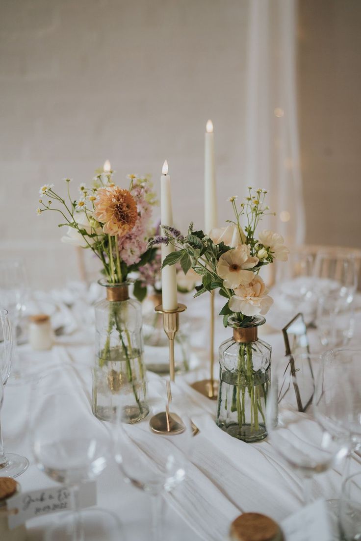 there are many vases with flowers and candles on the table
