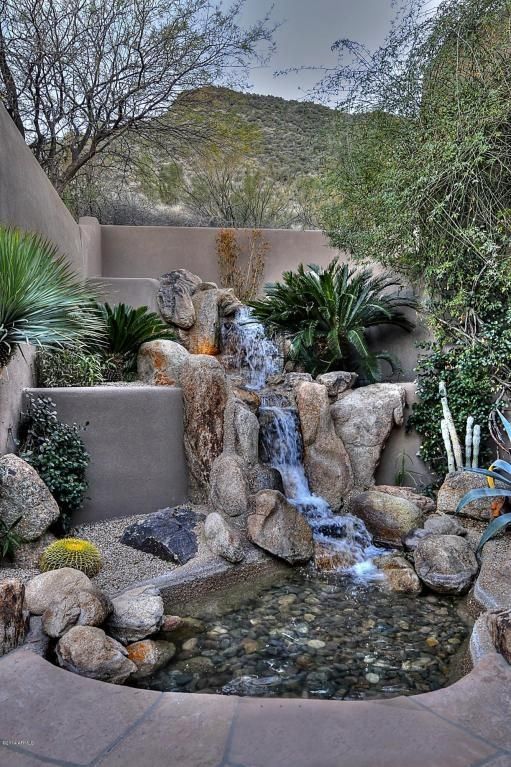 a small waterfall in the middle of a garden with rocks and plants on either side
