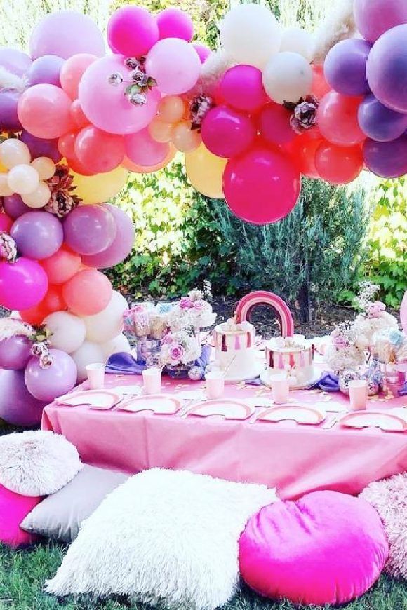 a table with balloons, cake and other items on it in the grass under an arch