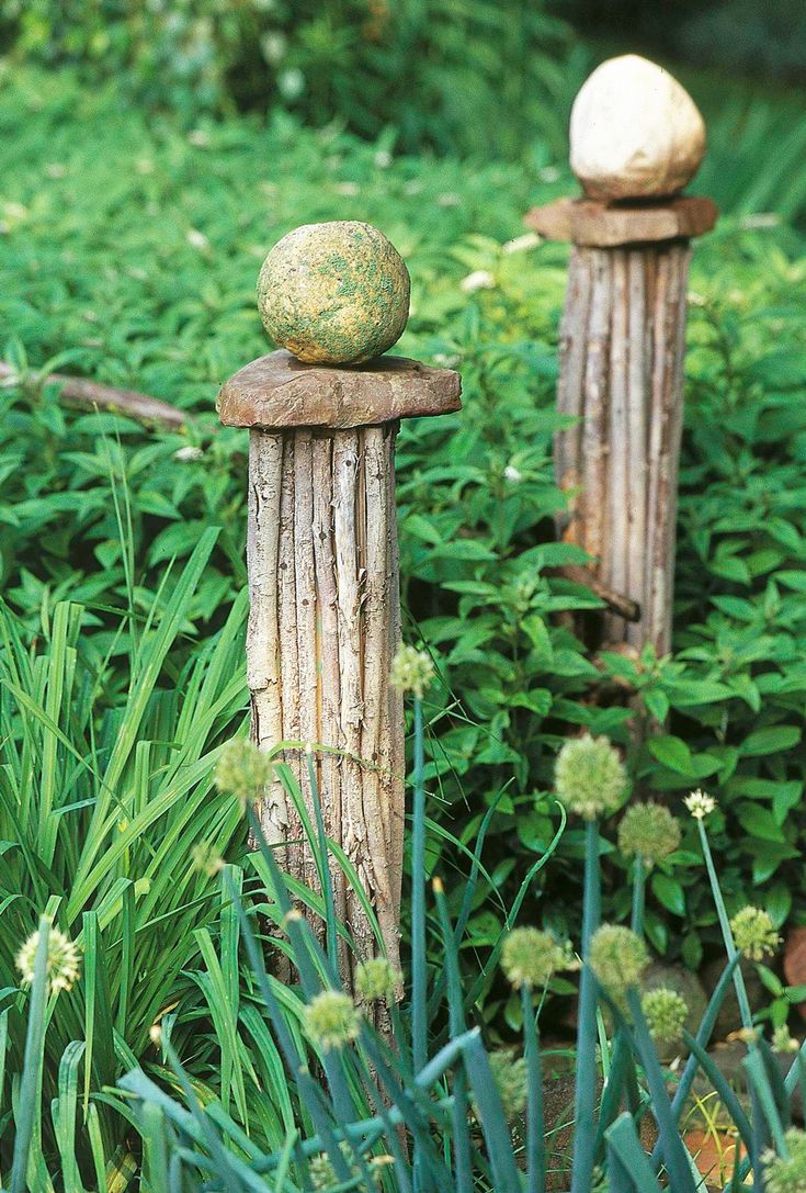 two wooden posts with balls on them are in the middle of some green plants and grass