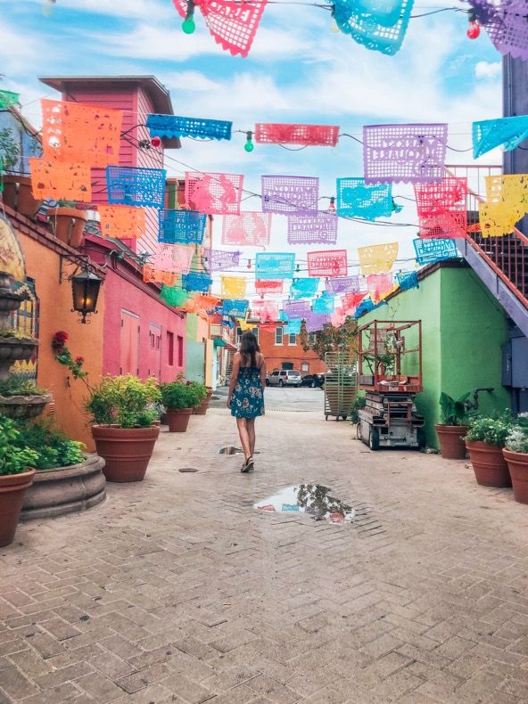 a woman is walking down an alley way with many colorful flags hanging from the buildings