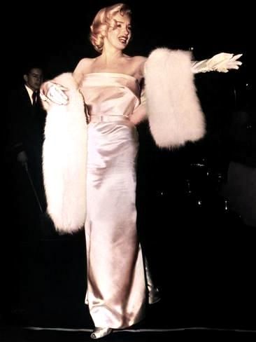 a woman in a white dress and fur stole with her arms spread out to the side