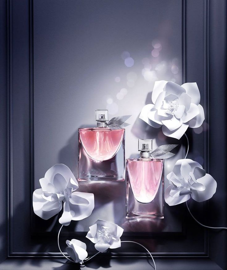 two perfume bottles with white flowers in front of them on a black table next to a mirror