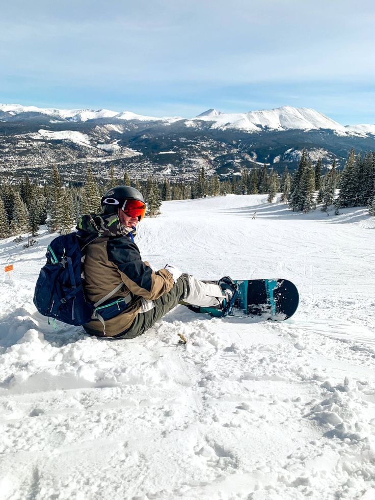 a snowboarder sitting in the snow on top of a mountain with his board