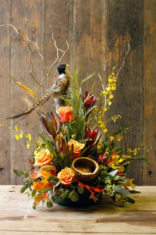 a vase filled with flowers sitting on top of a wooden table next to a bird