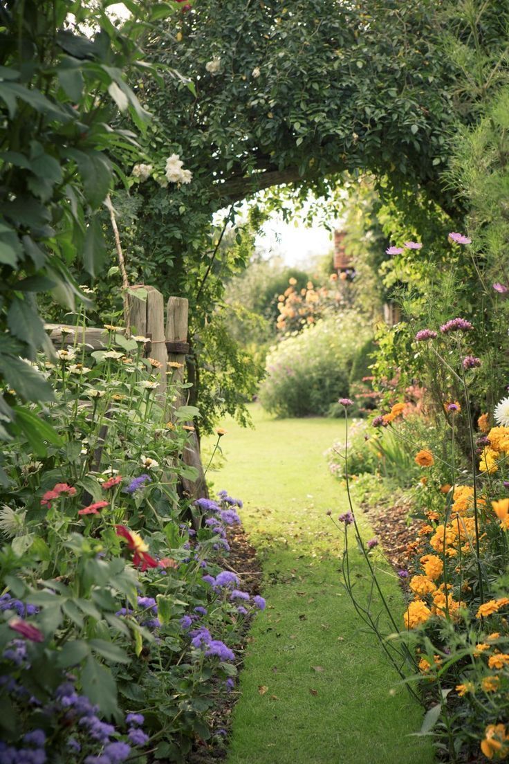a garden with lots of flowers and plants growing on either side of the path that leads to an open gate