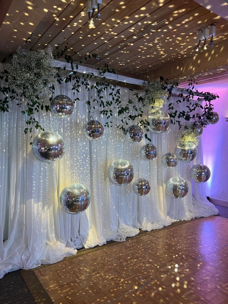 a room filled with lots of balloons and greenery hanging from the ceiling next to a white curtain