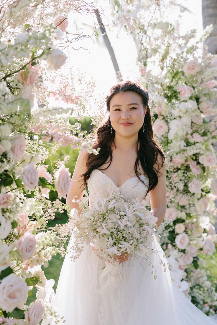 a woman in a wedding dress standing under a flower covered archway with flowers all around her