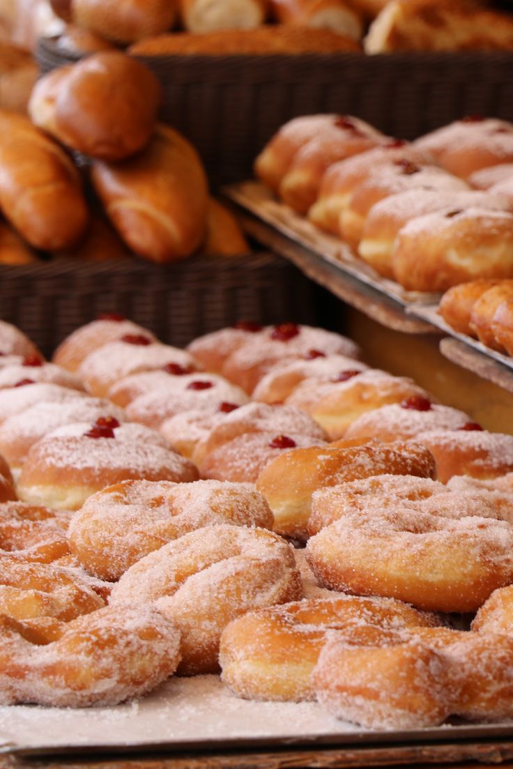many different types of doughnuts and pastries on display in trays at a bakery