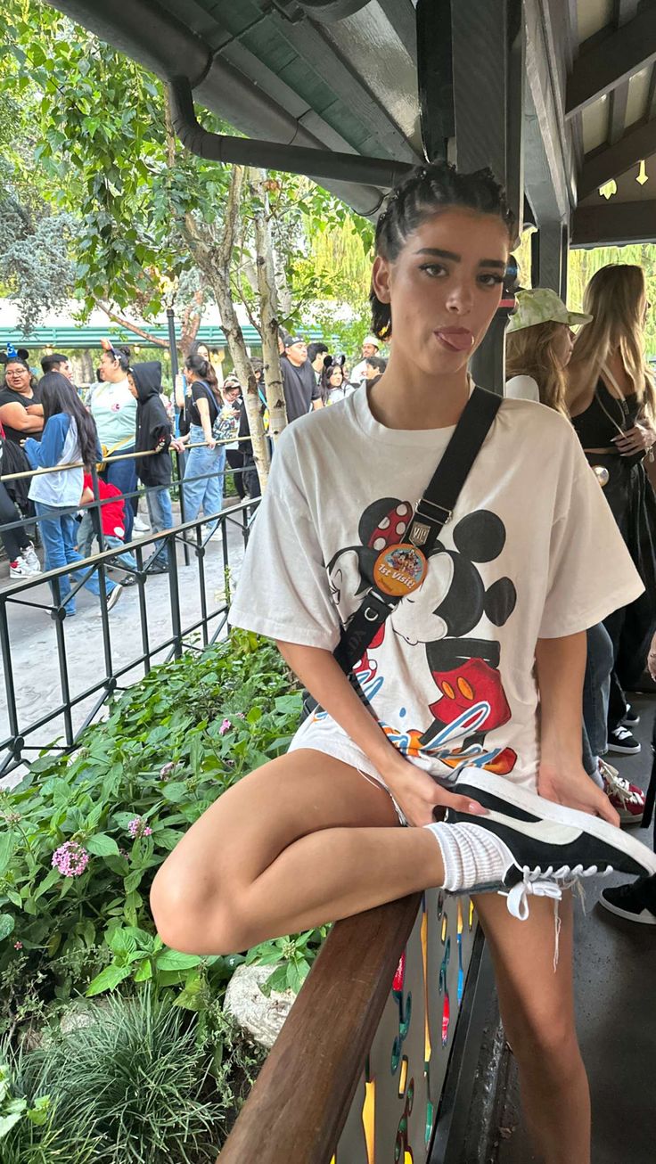 a woman sitting on a bench with her legs crossed and wearing mickey mouse t - shirt